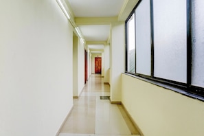 A corridor with a tiled floor, a window with a textured pattern, and a wooden door at the end. - Super Hotel O Pachgaon Near Kolhapur (Kolhapur)