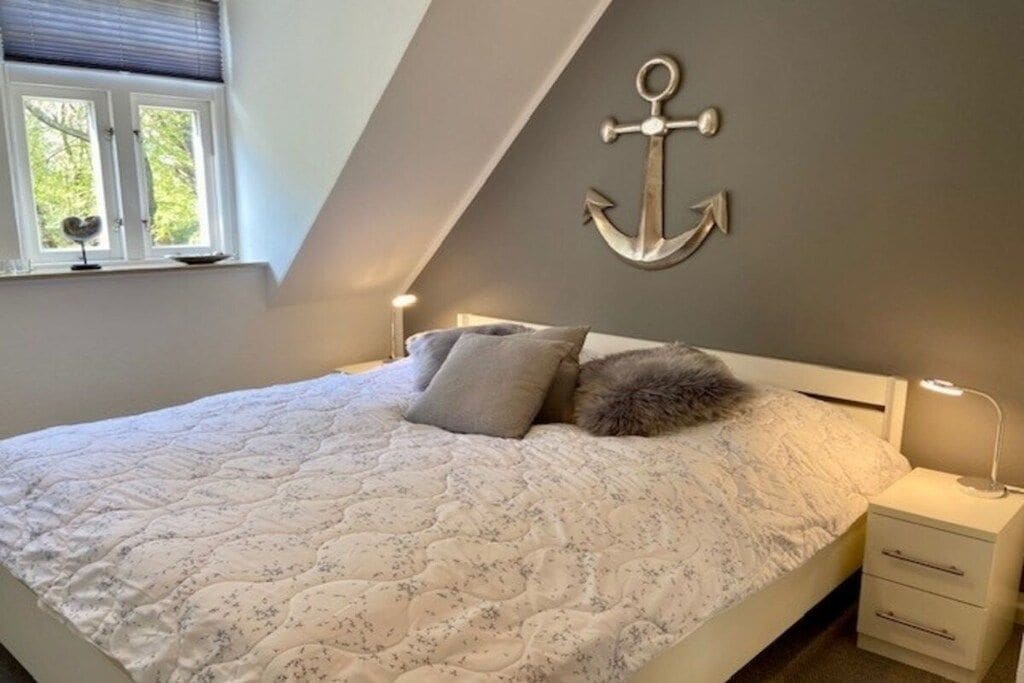 Un dormitorio con cama, almohadas, una mesita de noche, una lámpara y un adorno fijado a la pared.