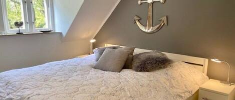 A bedroom with a bed, pillows, a nightstand, a lamp, and a wall-mounted anchor decoration.