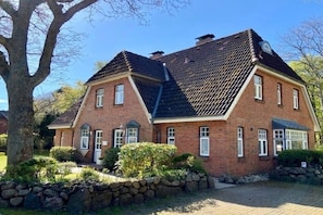 A two-story brick house with a steeply pitched roof, a stone wall surrounding the property, and a paved driveway. - Holiday apartment in Wyk on Föhr with Wi-Fi (Wyk auf Föhr)