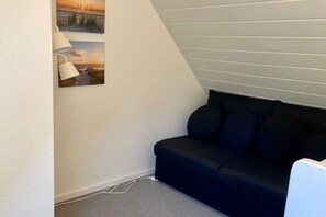 Ein Zimmer mit einem dunkelgrauen Sofa, einer Lampe und zwei gerahmten Bildern an der Wand.