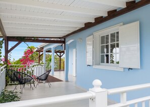 A covered outdoor area with a wooden deck, white railings, and a view of the sea. - Homerez - House Baillif (Baillif)