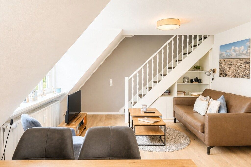 A modern living room with a staircase, a flat-screen TV, a sofa, and a dining area.