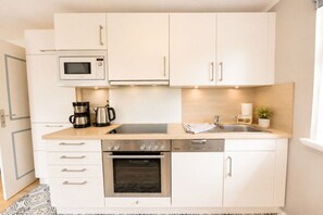 A modern kitchen with white cabinetry, a microwave, a coffee maker, an oven, and a dishwasher. - Holiday apartment Ankerplatz Wrixum (Wrixum auf Föhr)