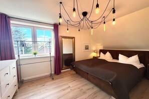 A bedroom with a large bed, a window with curtains, a mirror, and a chandelier. - Holiday home in Wyk with swimming pool (Wyk)