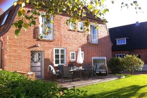 A brick house with a patio, outdoor seating, and a well-maintained lawn. - Holiday home in Föhr with 1 bedroom (Wyk auf Föhr)