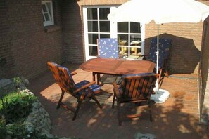 Eine Terrasse im Freien mit einem Holztisch und -stühlen, einem weißen Sonnenschirm und einer Ziegelwand.