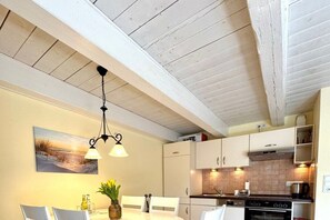Eine moderne Küche mit weißen Schränken, ein Essbereich mit Tisch und Stühlen sowie eine Decke mit freiliegenden Balken.