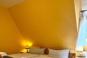 A room with a slanted ceiling, a bed with pillows, a nightstand with a lamp, and a window with curtains. - Holiday home in Föhr with 1 bedroom (Wyk auf Föhr)