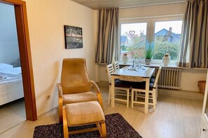 Un dormitorio con cama, una silla, una mesa de comedor y un ventanal con cortinas.