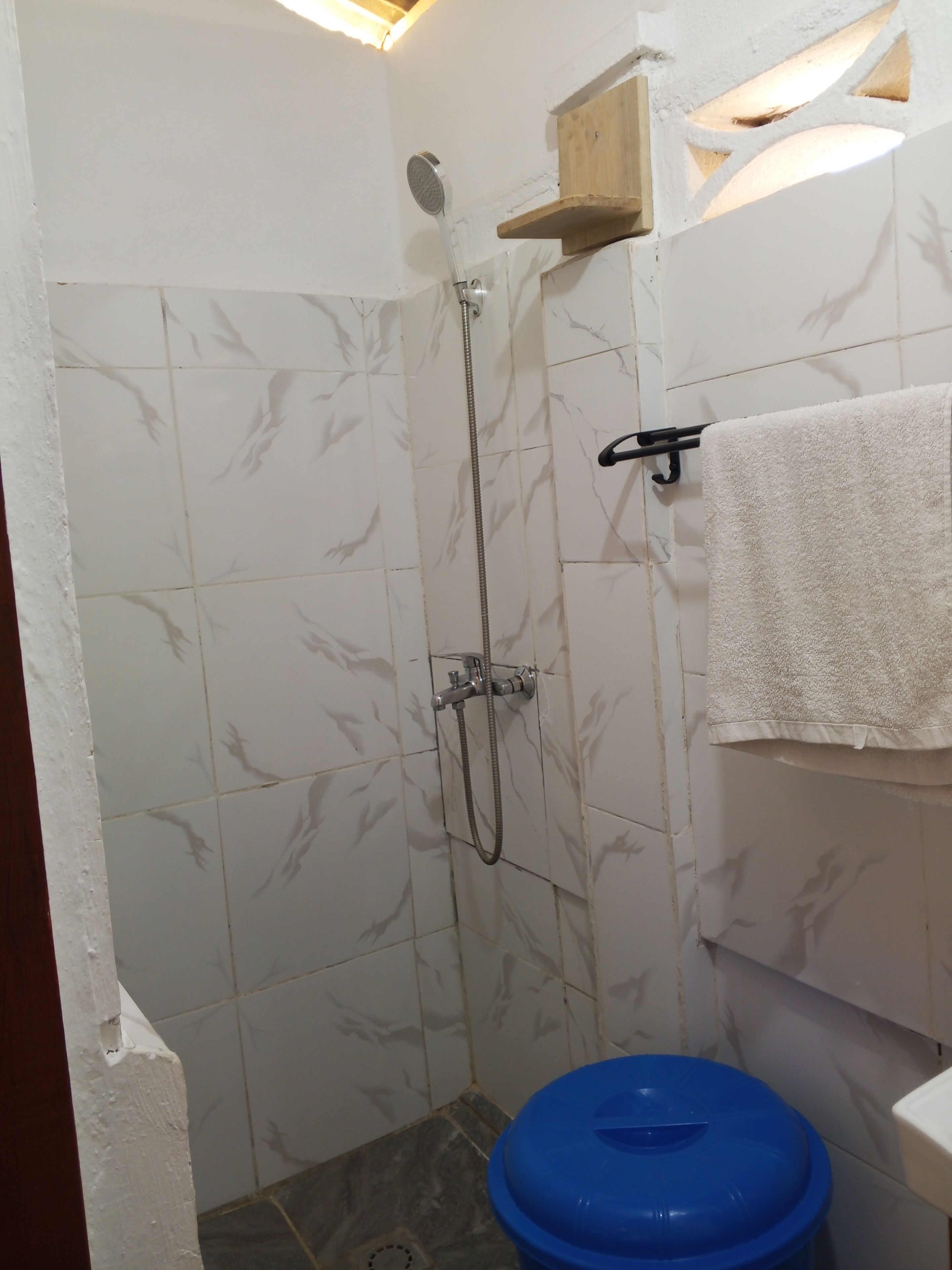 A bathroom with a shower, a white towel hanging on a rack, and a blue trash bin.