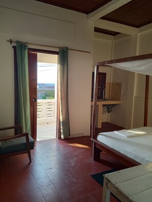 Ein Zimmer mit einem Bett, einem Sessel, einem Tisch und einer Tür zu einem Außenbereich.