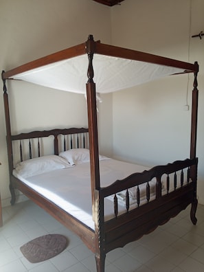 A four-poster canopy bed with a wooden frame and white bedding. - GOLDEN WAVE HOTEL (Mahajanga)