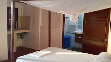 A single-bed room with a wooden frame, a canopy bed, a bedside table, and a view of a bathroom with a sink and mirror.