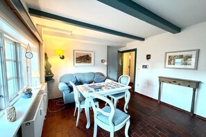 A room with a dining table and chairs, a sofa, a radiator, and a wall-mounted lamp. - Holiday apartment in Föhr with 2 bedrooms (Nieblum)