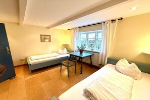 Quarto com cama, escrivaninha, cadeira e janela com cortinas.