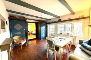A room with a dining table, chairs, a sofa, and a window with a view. - Holiday apartment in Föhr with 2 bedrooms (Nieblum)