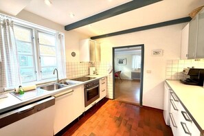 A kitchen with a dishwasher, stove, and sink. There is a window with curtains, and a door leading to another room. - Holiday apartment in Föhr with 2 bedrooms (Nieblum)