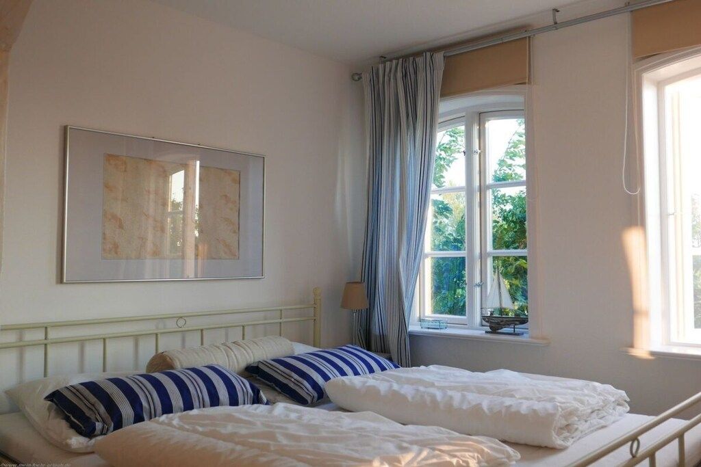 Una camera da letto con un letto, una finestra con tende, un comodino e un quadro appeso al muro.