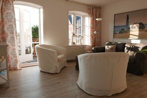 A living room with a sofa, armchairs, a radiator, a window with curtains, and a painting on the wall. - Holiday apartment in Föhr with 1 bedroom (Oldsum)