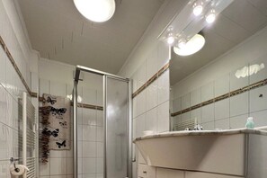 Een badkamer met een douchecabine van glas, een wastafel met spiegel en een handdoekrek met een handdoek met vlindermotief.
