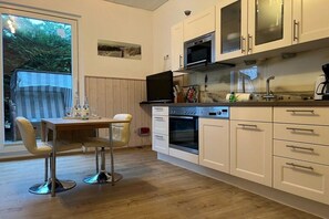 Una cocina moderna con armarios blancos, horno empotrado y comedor con mesa y sillas.