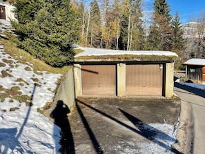 A garage with a snow-covered roof, adjacent to a road with snow patches. - Chalet Felsenberg (CharmingStay), (Flumserberg Tannenheim), by Interhome (Flumserberg Tannenheim)