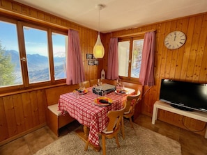A cozy dining area with a checkered tablecloth, wooden chairs, and a view of mountains through large windows. - Chalet Felsenberg (CharmingStay), (Flumserberg Tannenheim), by Interhome (Flumserberg Tannenheim)