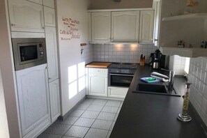 Eine Küche mit weißen Schränken, einer Mikrowelle, einem Backofen und einer Kaffeemaschine.