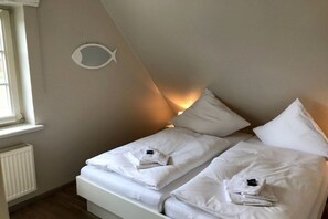 Ein Einzelbett mit weißer Bettwäsche und Kissen, eine runde Wanddekoration sowie ein Fenster mit Heizkörper.