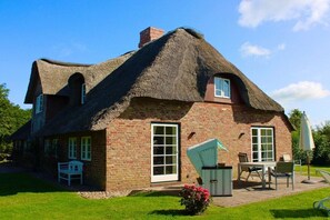 Une maison à toit de chaume, avec une façade en briques, une porte et une fenêtre.