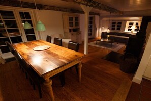 A dining area with a wooden table and chairs, a cabinet, and a sofa in the background. - Holiday home in Borgsum with swimming pool (Borgsum)