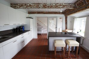 A kitchen with white cabinets, a dark countertop, and a rustic ceiling. There is a small island with stools and a window with a view. - Holiday home in Borgsum with swimming pool (Borgsum)