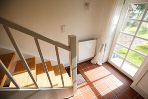 Un escalier avec des marches en bois et des rampes blanches menant à une pièce équipée d’un radiateur et d’une fenêtre donnant sur un paysage verdoyant.