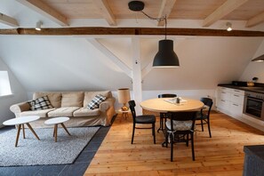 Una habitació acollidora amb sostre de fusta, una taula rodona amb cadirees, un sofà amb coixins i una làmpada.
