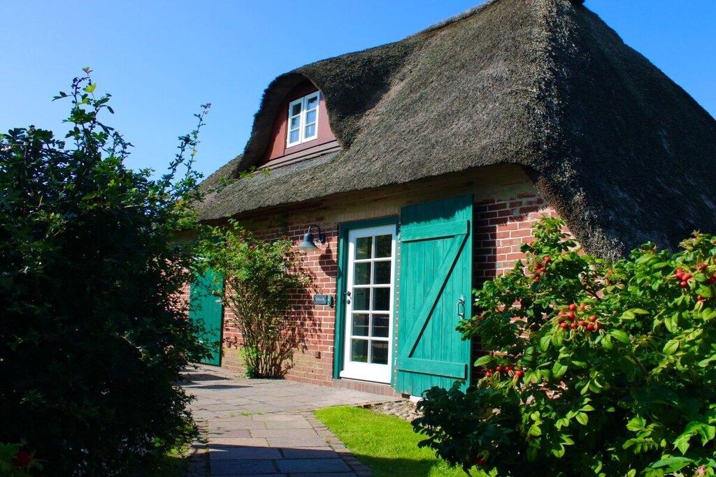 A traditional thatched-roof house with a brick exterior, a visible window, and green shutters.