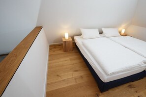 Ein Schlafzimmer mit Holzboden, einem Bett mit weißer Bettwäsche und zwei Nachttischen mit Lampen.