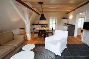 A modern interior with a sofa, dining table, chairs, a white armchair, a kitchen area, and a television. - Holiday home in Borgsum with swimming pool (Borgsum)