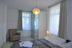 A hotel room with a bed, a chair, a bedside table with a lamp, and a large mirror. - Holiday apartment with 1 bedroom (Wyk auf Föhr)