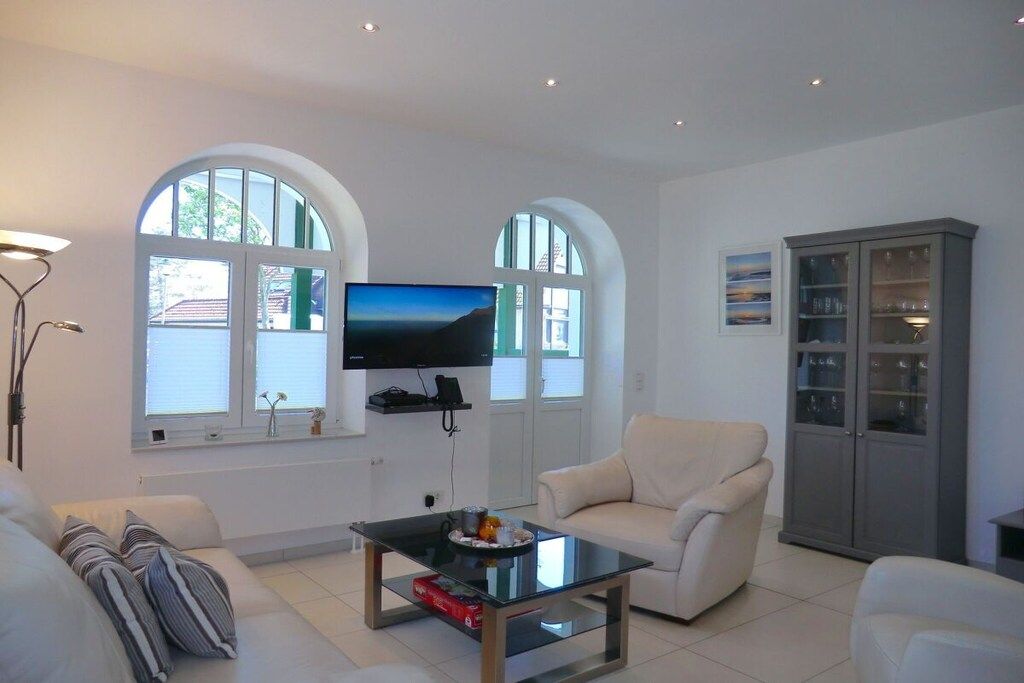 A living room with a flat-screen TV mounted on the wall, two arched windows, a sofa, a coffee table, and a cabinet.