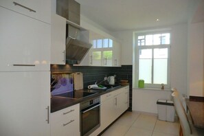 A modern kitchen with white cabinets, a stainless steel range hood, and a window providing natural light. - Holiday apartment with 1 bedroom (Wyk auf Föhr)