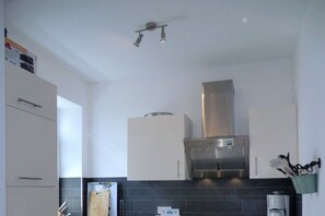 A kitchen with white cabinets, a stainless steel range hood, and a black tiled backsplash. - Holiday apartment with 1 bedroom (Wyk auf Föhr)