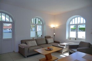 A modern living room with a sofa, a coffee table, and two armchairs. There are arched windows providing natural light. - Holiday apartment with 1 bedroom (Wyk auf Föhr)