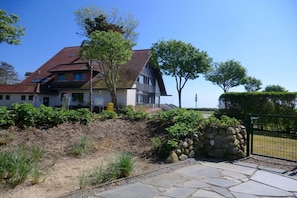 A two-story house with a red-tiled roof, a stone wall, and a paved driveway. - Holiday apartment with 1 bedroom (Wyk auf Föhr)