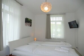 A hotel room with a bed, a bedside lamp, a television mounted on the wall, and a window with curtains. - Holiday apartment with 1 bedroom (Wyk auf Föhr)