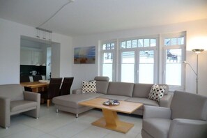 A modern living room with a sofa, armchairs, a coffee table, and a dining area with chairs and a table. - Holiday apartment with 1 bedroom (Wyk auf Föhr)