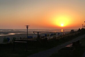 A sunset over a beach with a pier extending into the water, a walkway, and benches. - Holiday apartment with 1 bedroom (Wyk auf Föhr)