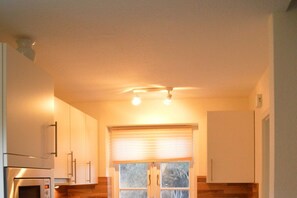 A kitchen with a built-in oven, cabinets, and a window with blinds. - Green Eilun - House Section 5 (Wyk auf Föhr)