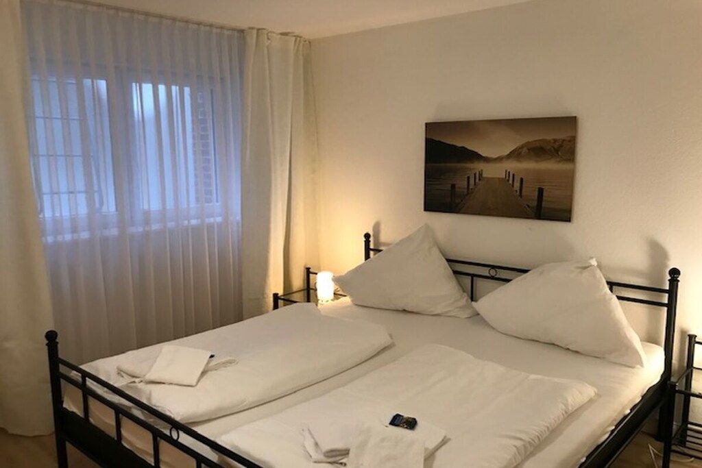 A double bed with white linens, a bedside table with a lamp, and a painting on the wall.