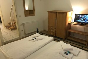 Quarto de hotel com cama, guarda-roupa de madeira, televisão e espelho.